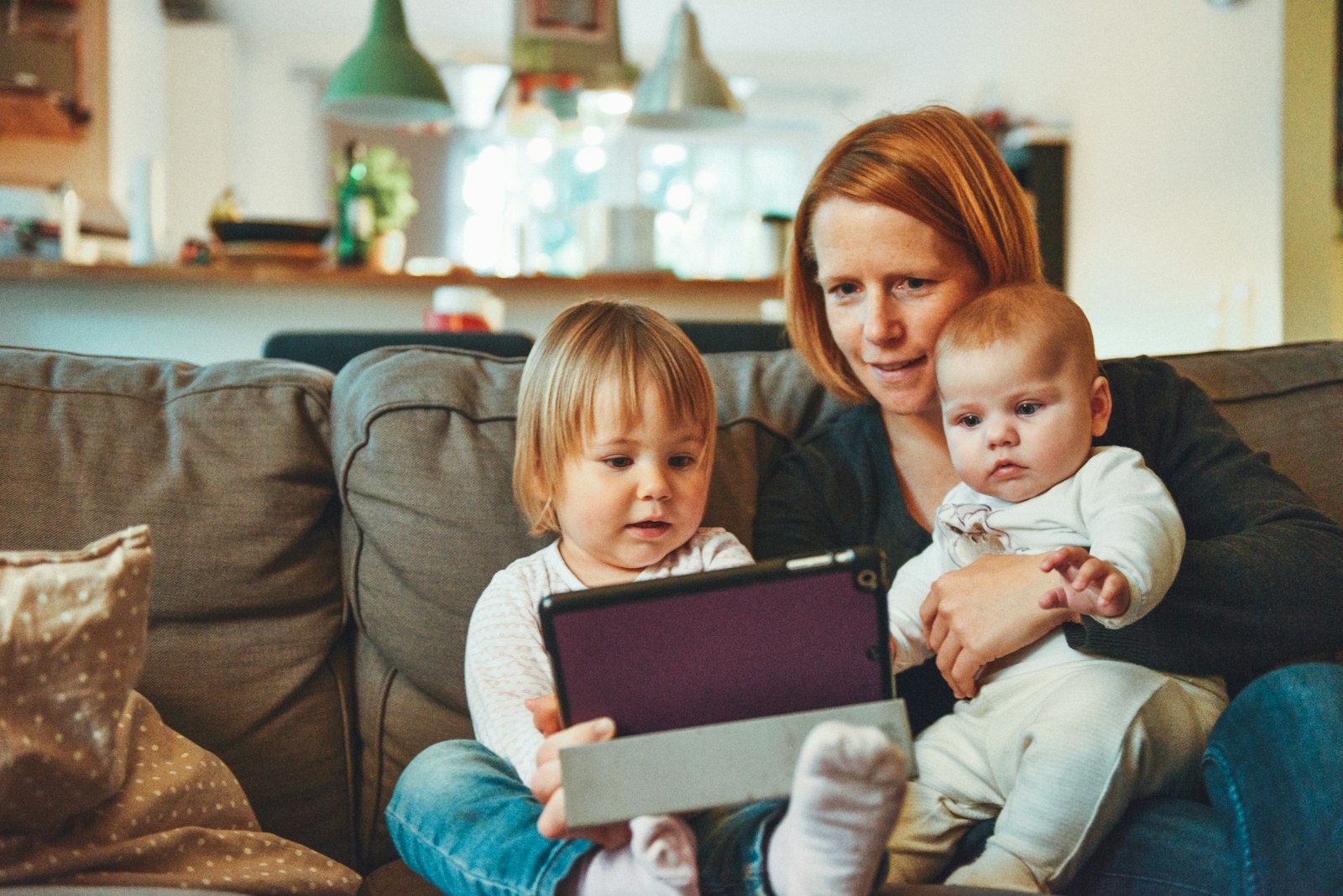 A mom on the couch with her two little kids looking at a tablet together