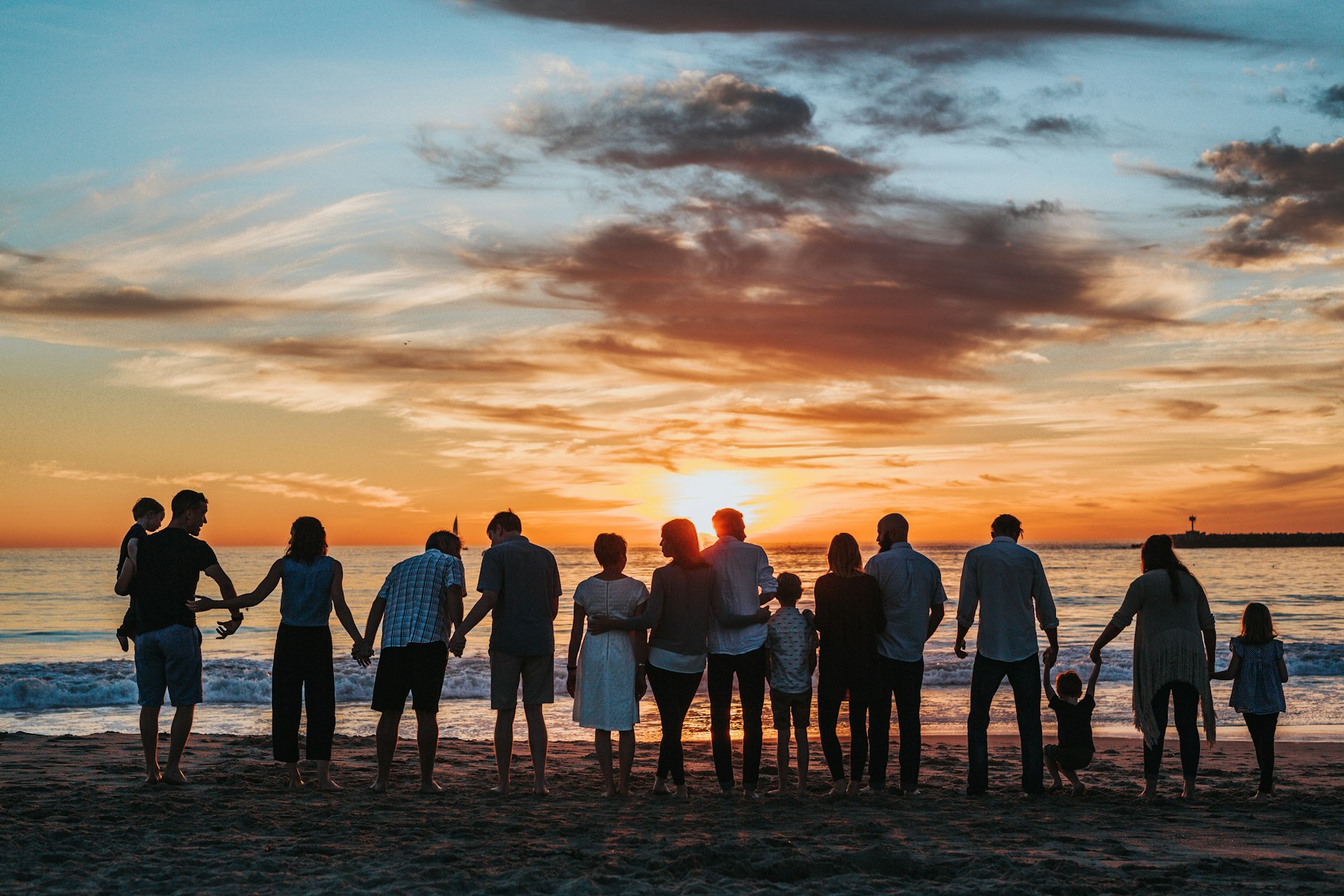 A large multi-generational family holding hands on the beach at sunset