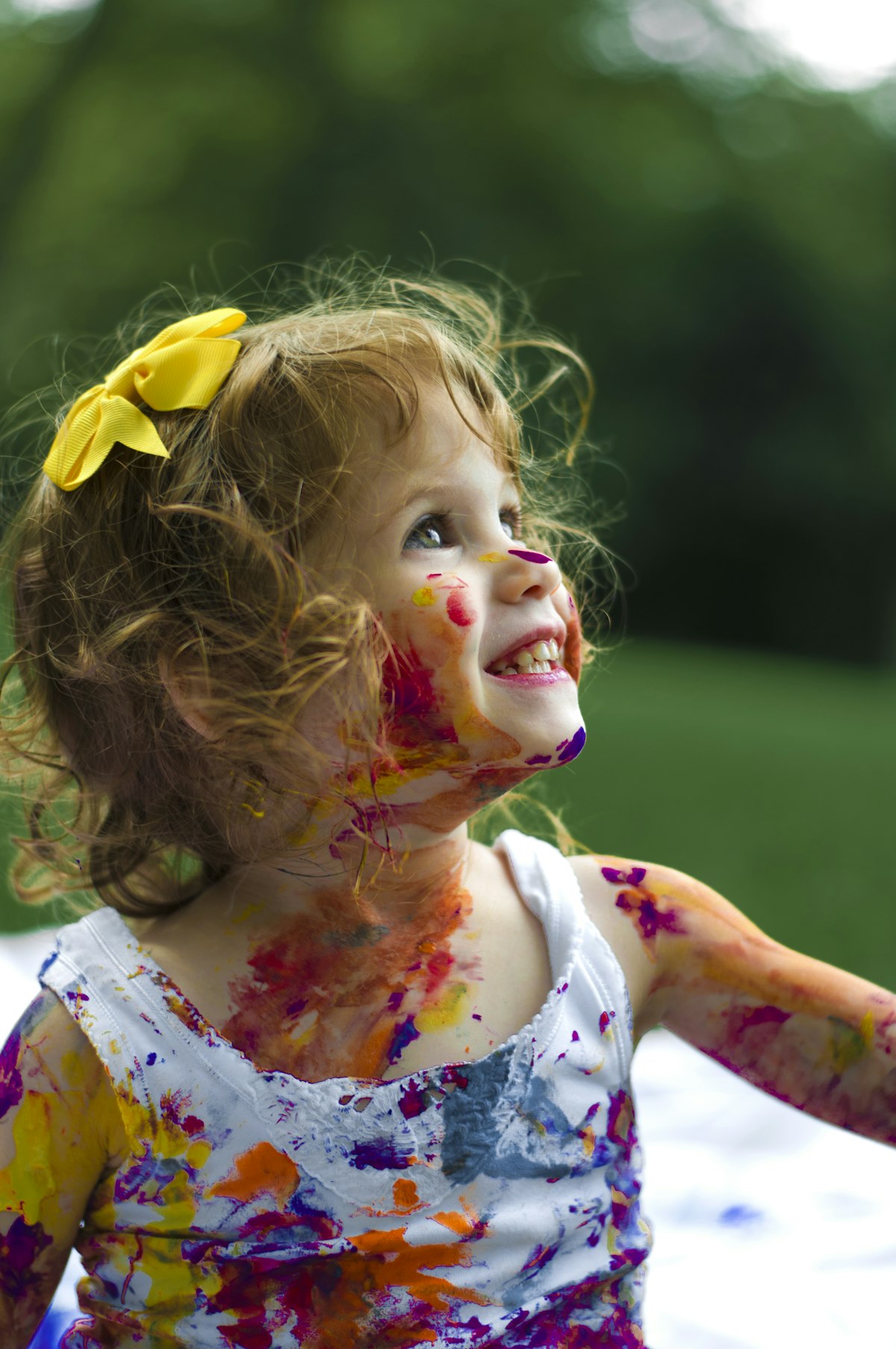A little girl covered in paint laughing outdoors