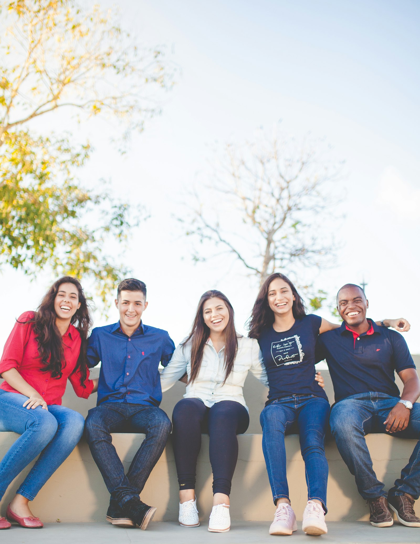 Five smiling teenagers sitting together outside