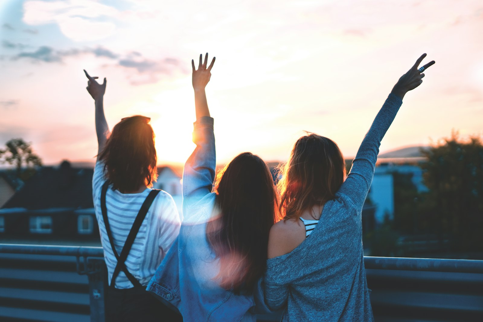 Three teenagers with their arms raised celebrating at sunset on a rooftop